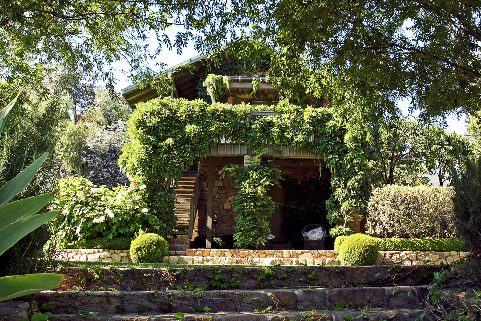 На фото: двухэтажный, зеленый частный загородный дом в средиземноморском стиле с облицовкой из камня и двускатной крышей с