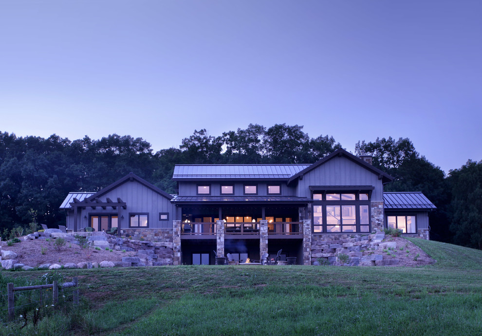 Immagine della villa grande grigia country a due piani con rivestimento in legno, tetto a capanna e copertura in metallo o lamiera