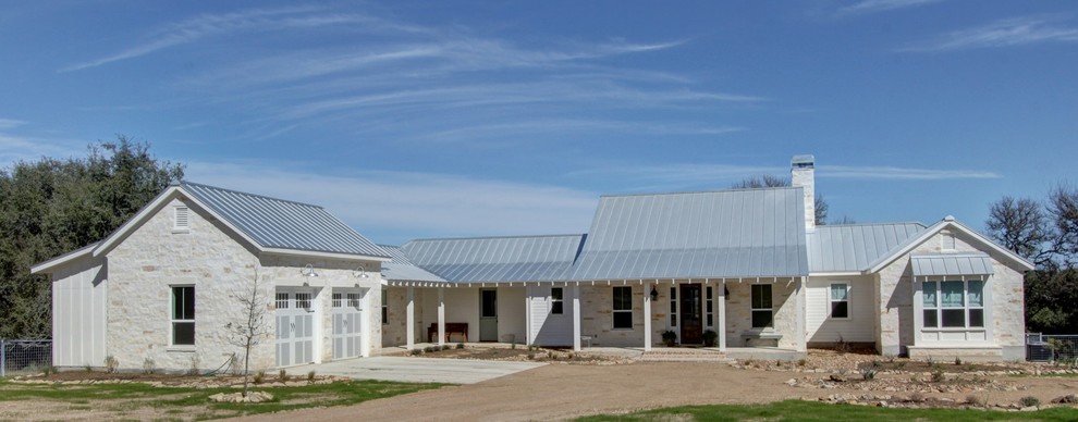 This is an example of a white farmhouse bungalow house exterior in Austin with stone cladding.