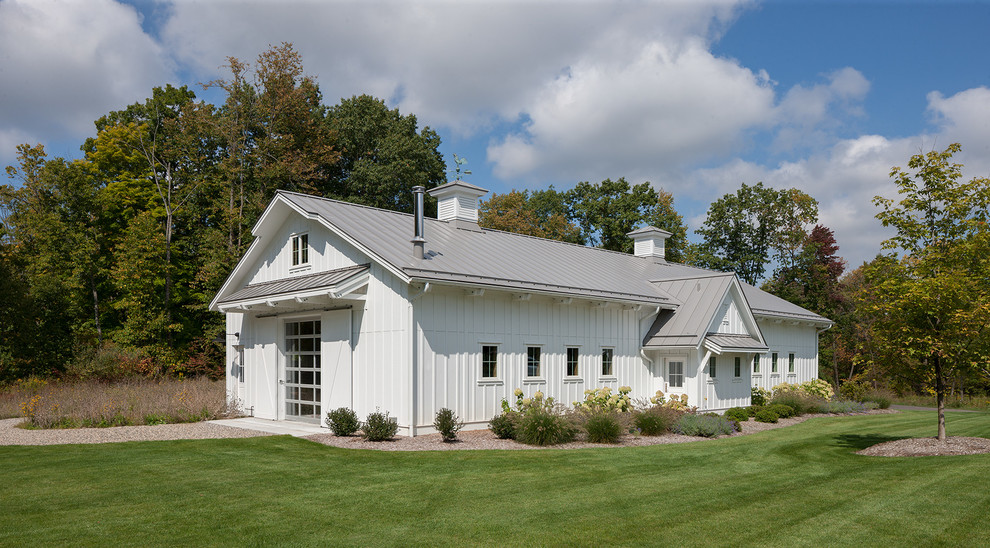 Foto della facciata di una casa grande bianca country a un piano con rivestimento con lastre in cemento, tetto a capanna e copertura in metallo o lamiera