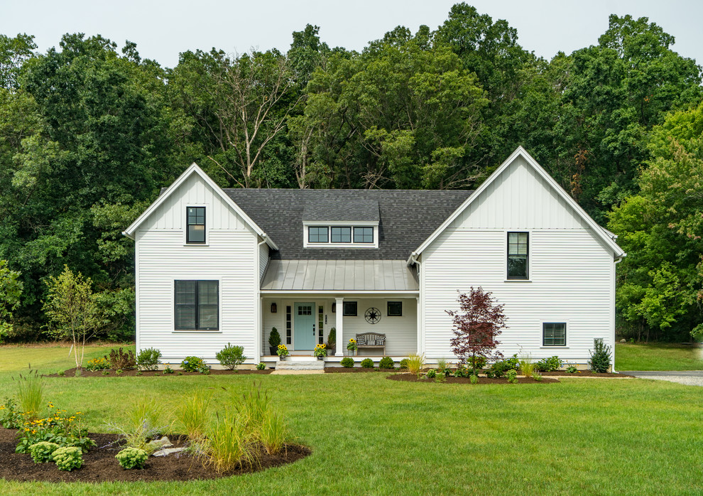 Foto della villa bianca country a due piani con rivestimento in legno, tetto a capanna e copertura a scandole