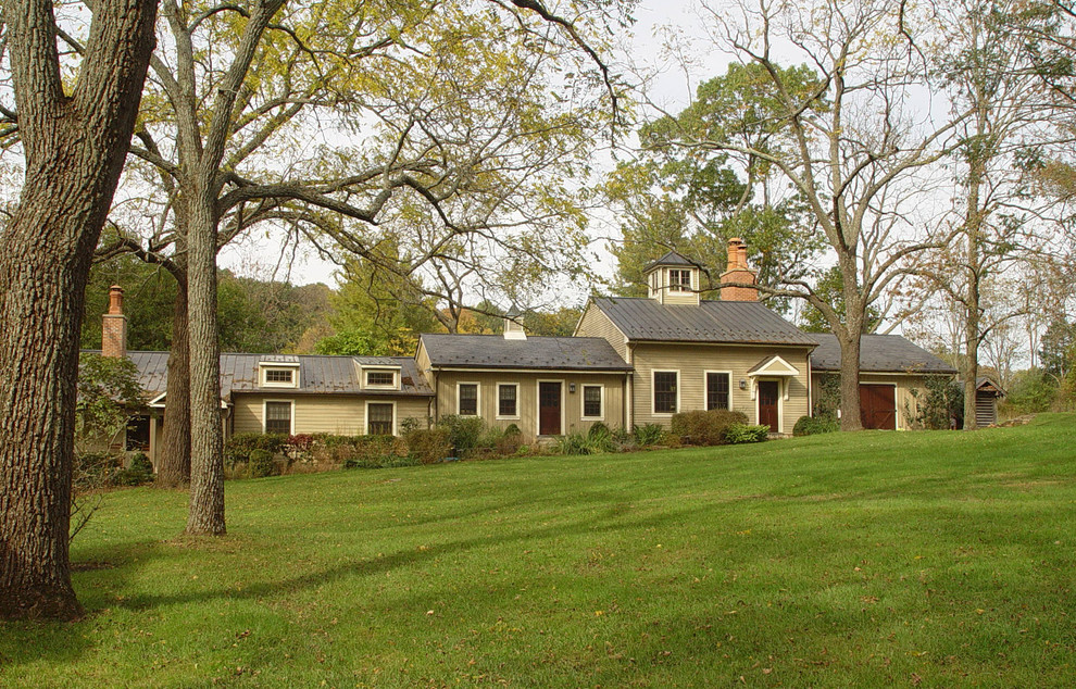 Réalisation d'une grande façade de maison beige champêtre de plain-pied avec un revêtement en vinyle, un toit à deux pans et un toit en métal.