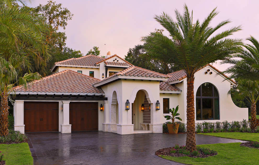Cette image montre une façade de maison beige méditerranéenne en stuc de taille moyenne et à un étage avec un toit à quatre pans et un toit en tuile.