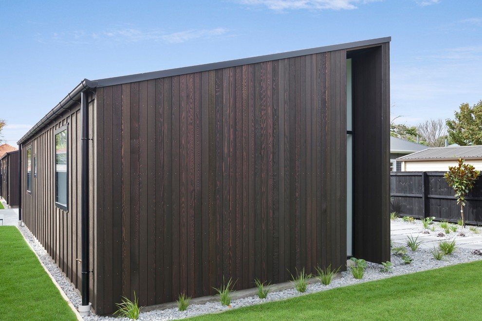 Cette image montre une façade de maison noire design en bois de taille moyenne et de plain-pied avec un toit plat et un toit en métal.