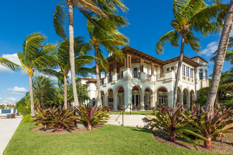 Immagine della facciata di una casa ampia beige tropicale a due piani con tetto piano e rivestimento in stucco