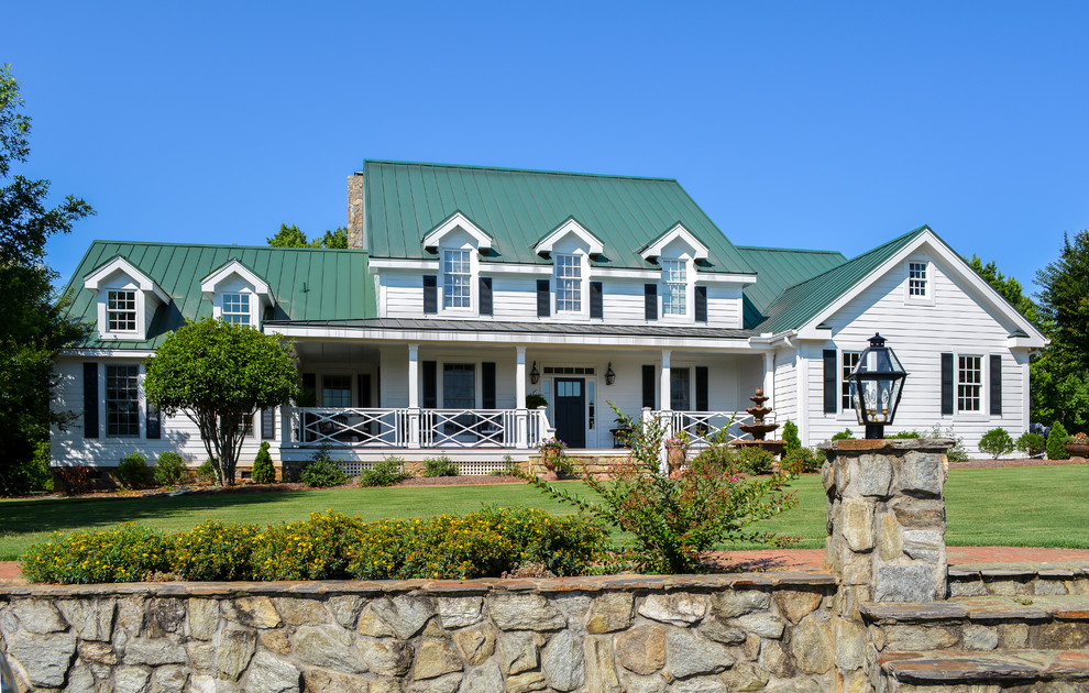 Imagen de fachada de casa blanca campestre grande de una planta con revestimiento de aglomerado de cemento, tejado a dos aguas y tejado de metal