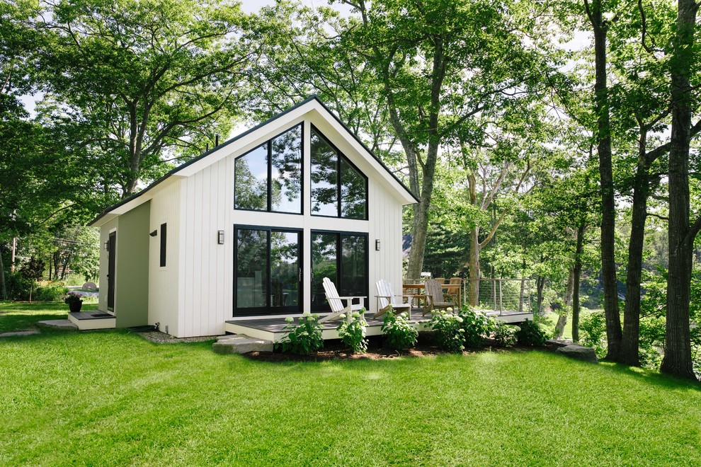 На фото: маленький, двухэтажный, белый мини дом в стиле кантри с металлической крышей и двускатной крышей для на участке и в саду
