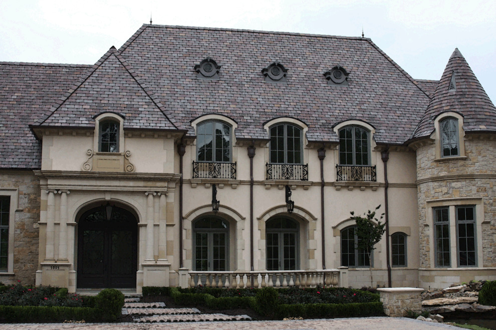 Cette photo montre une très grande façade de maison beige chic en stuc à un étage avec un toit en tuile.