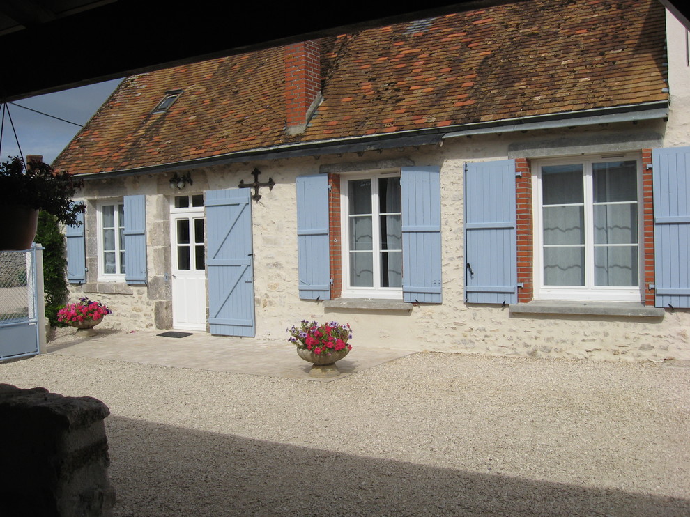 Esempio della facciata di una casa piccola beige country a un piano con rivestimento in stucco e tetto a capanna