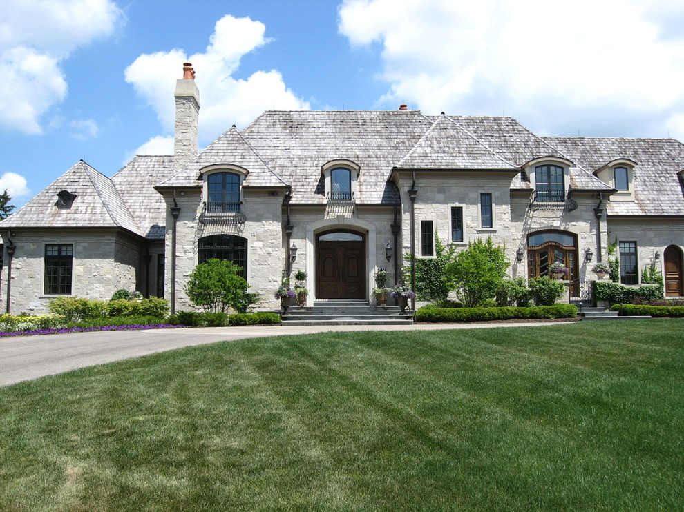 Пример оригинального дизайна: двухэтажный, серый, огромный частный загородный дом в классическом стиле с облицовкой из камня, вальмовой крышей и крышей из гибкой черепицы