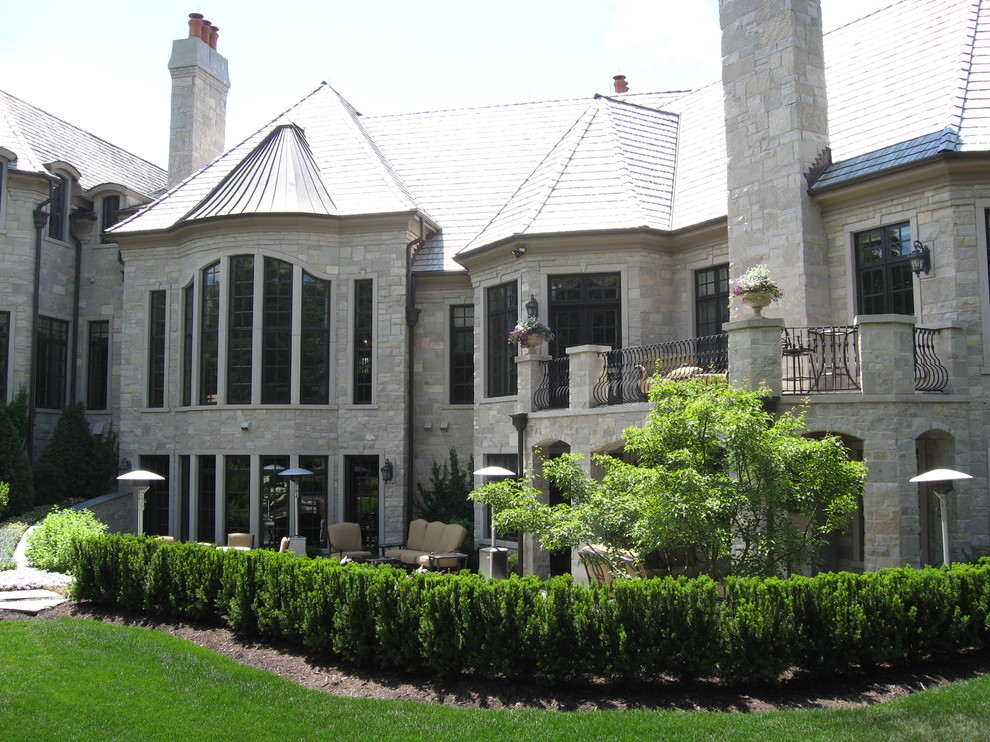 Réalisation d'une grande façade de maison grise tradition en pierre à un étage avec un toit à quatre pans.