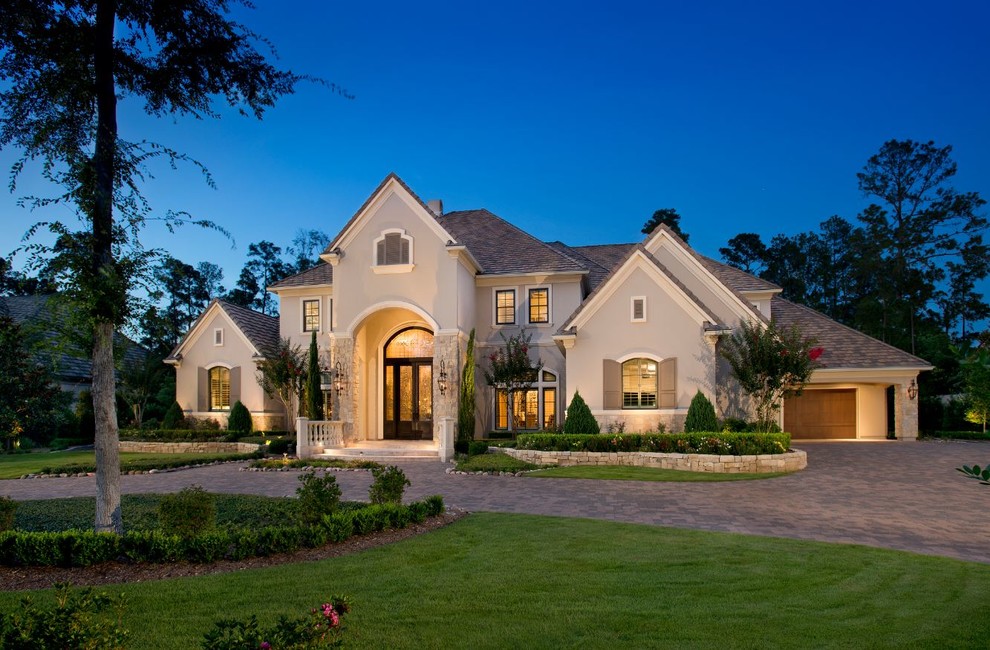 Large elegant beige two-story stucco house exterior photo in Houston with a hip roof and a shingle roof