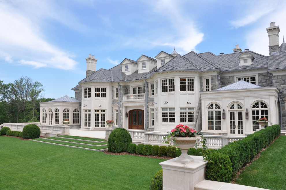 Huge elegant gray three-story stone house exterior photo in New York with a hip roof and a shingle roof