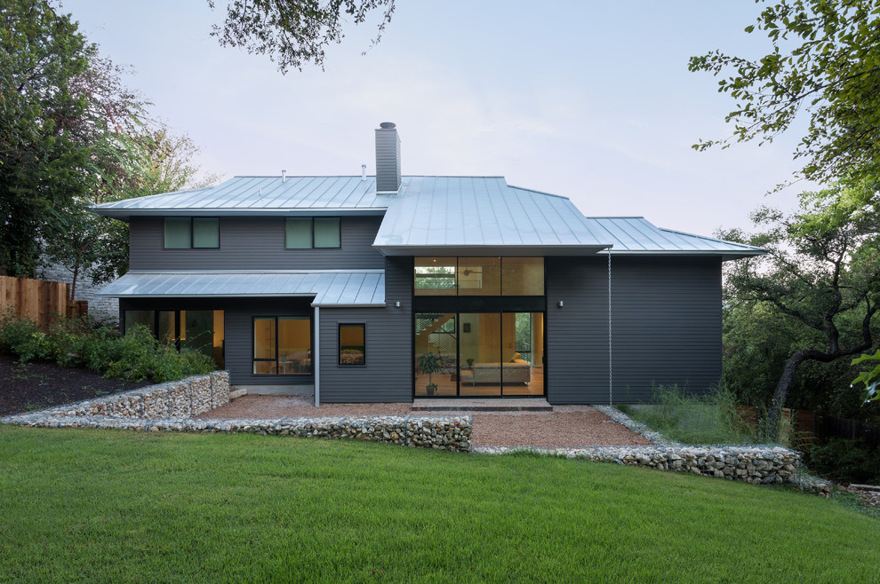 Aménagement d'une façade de maison grise contemporaine à un étage avec un revêtement en vinyle, un toit à quatre pans et un toit en métal.