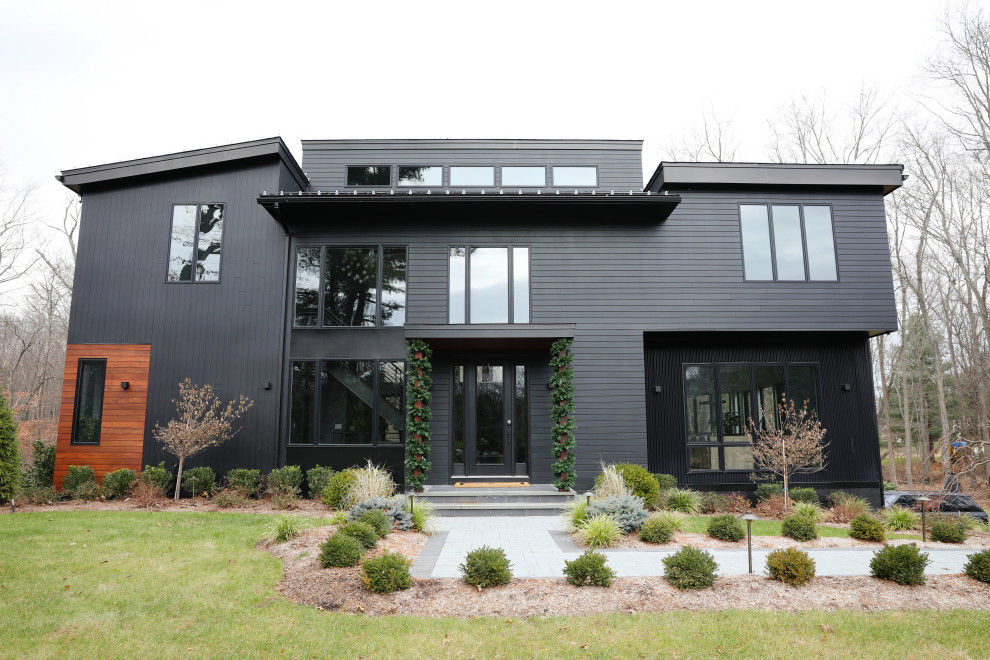 Diseño de fachada de casa negra actual de tamaño medio de dos plantas con revestimientos combinados, tejado de un solo tendido y tejado de metal