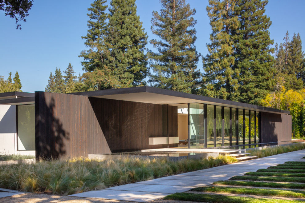 Diseño de fachada de casa marrón moderna grande de una planta con revestimiento de madera y tejado plano