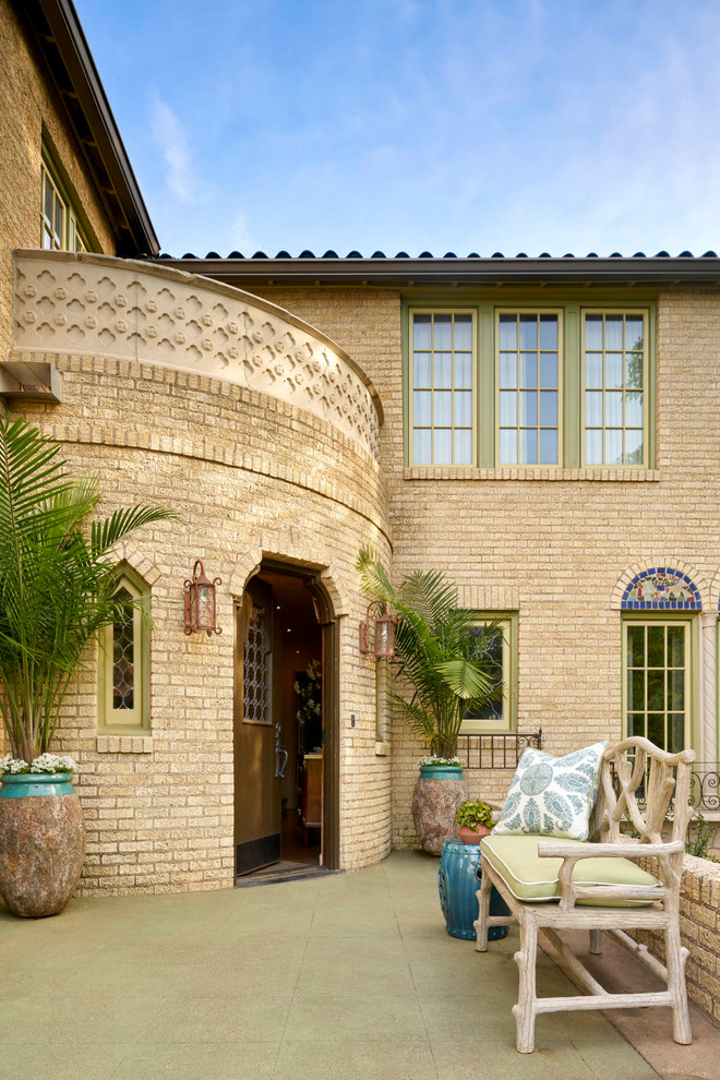Esempio della villa grande beige mediterranea a tre piani con rivestimento in mattoni, copertura in tegole e tetto a padiglione