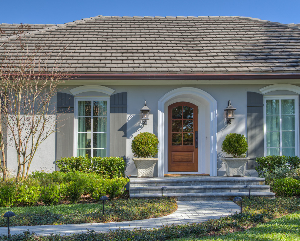 Ejemplo de fachada de casa gris clásica de tamaño medio de una planta con revestimiento de estuco, tejado a cuatro aguas y tejado de teja de barro