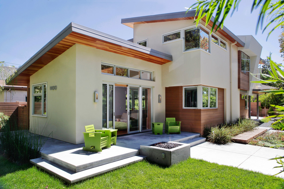 Idées déco pour une grande façade de maison beige moderne en stuc à un étage avec un toit plat et un toit gris.
