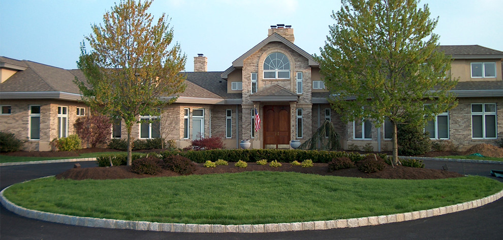 Large and beige traditional two floor house exterior in Other with stone cladding and a hip roof.
