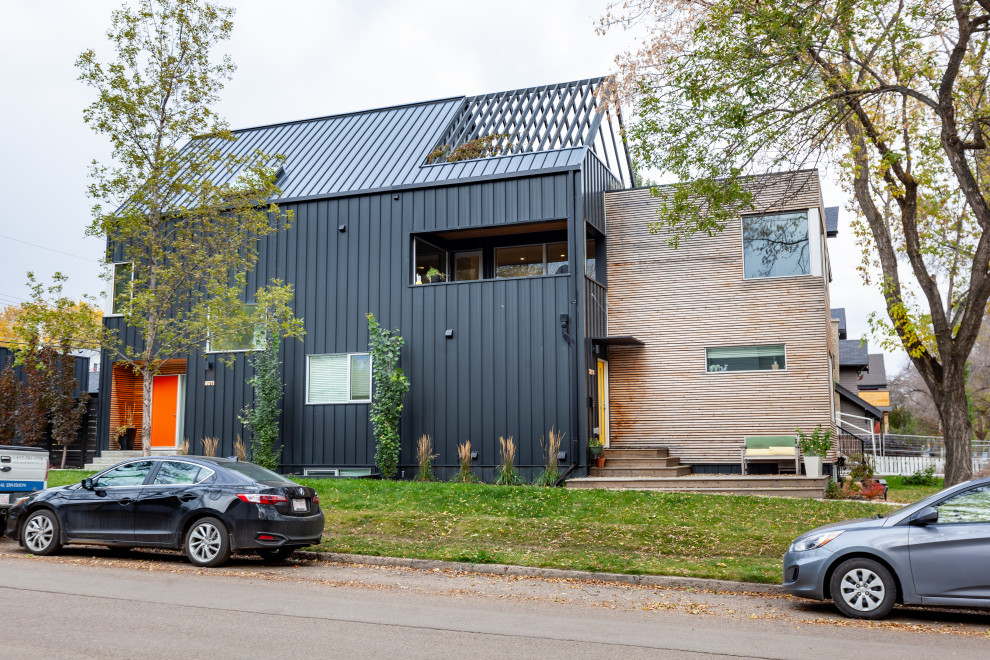 Foto della facciata di una casa bifamiliare nera moderna a tre piani di medie dimensioni con rivestimento in legno, tetto a capanna e copertura in metallo o lamiera