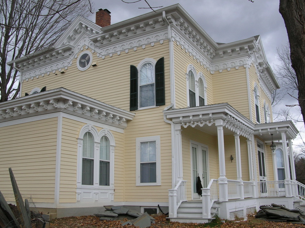 Esempio della facciata di una casa gialla vittoriana a tre piani con rivestimento in legno e tetto a capanna