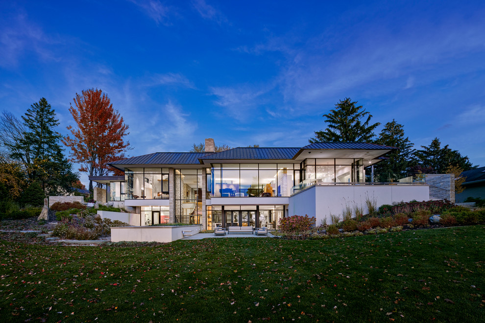 Foto della villa grande bianca contemporanea a due piani con rivestimento in vetro, tetto a padiglione e copertura in metallo o lamiera