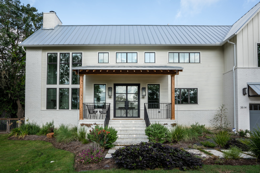 Ejemplo de fachada de casa blanca de estilo de casa de campo grande de dos plantas con revestimiento de ladrillo, tejado a dos aguas y tejado de metal