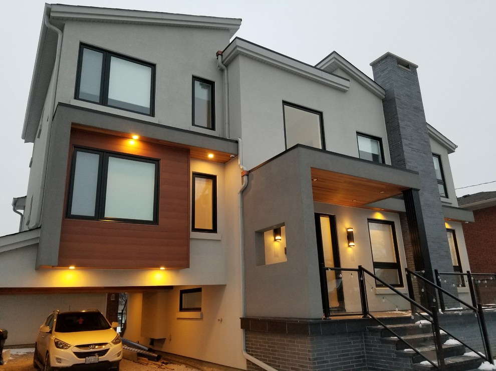 Cette image montre une grande façade de maison grise minimaliste en stuc à niveaux décalés avec un toit plat et un toit mixte.