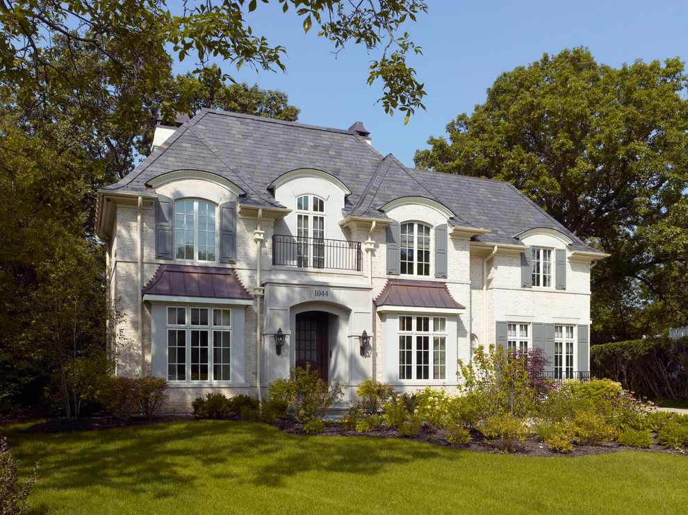 Стильный дизайн: двухэтажный, бежевый дом в классическом стиле с облицовкой из камня и вальмовой крышей - последний тренд