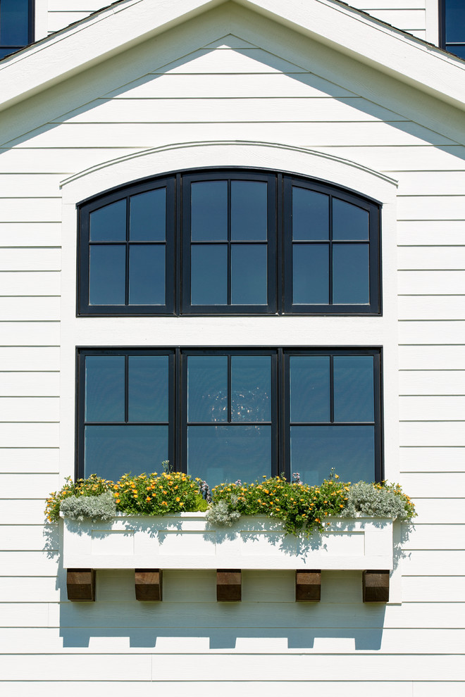 Cette photo montre une grande façade de maison blanche chic en panneau de béton fibré à un étage avec un toit à quatre pans et un toit en shingle.