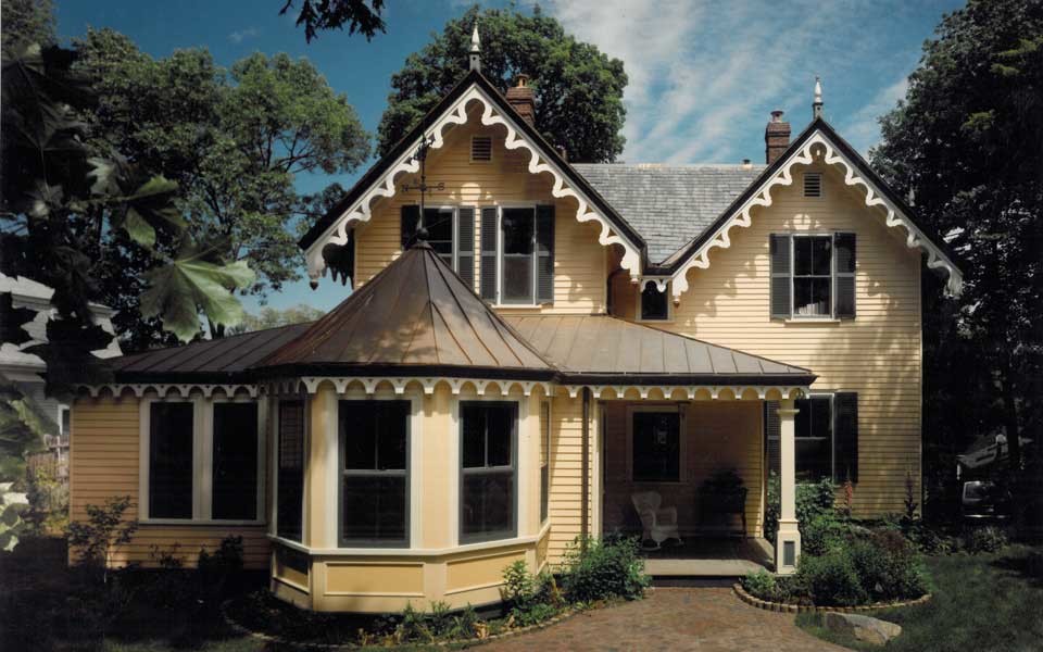 Diseño de fachada de casa amarilla bohemia de dos plantas con revestimiento de madera y tejado a dos aguas