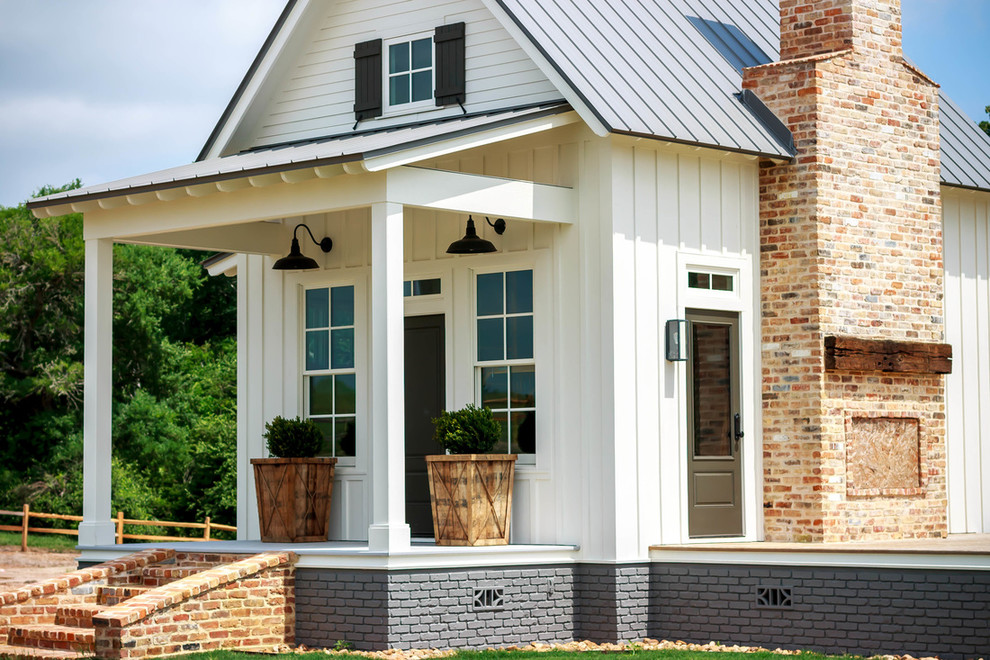 Immagine della micro casa bianca country a due piani di medie dimensioni con rivestimento in vinile, tetto a capanna e copertura in metallo o lamiera