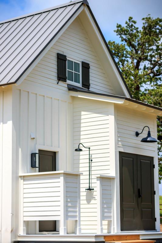 Réalisation d'une façade de maison blanche champêtre de taille moyenne et à un étage avec un revêtement en vinyle, un toit à deux pans et un toit en métal.