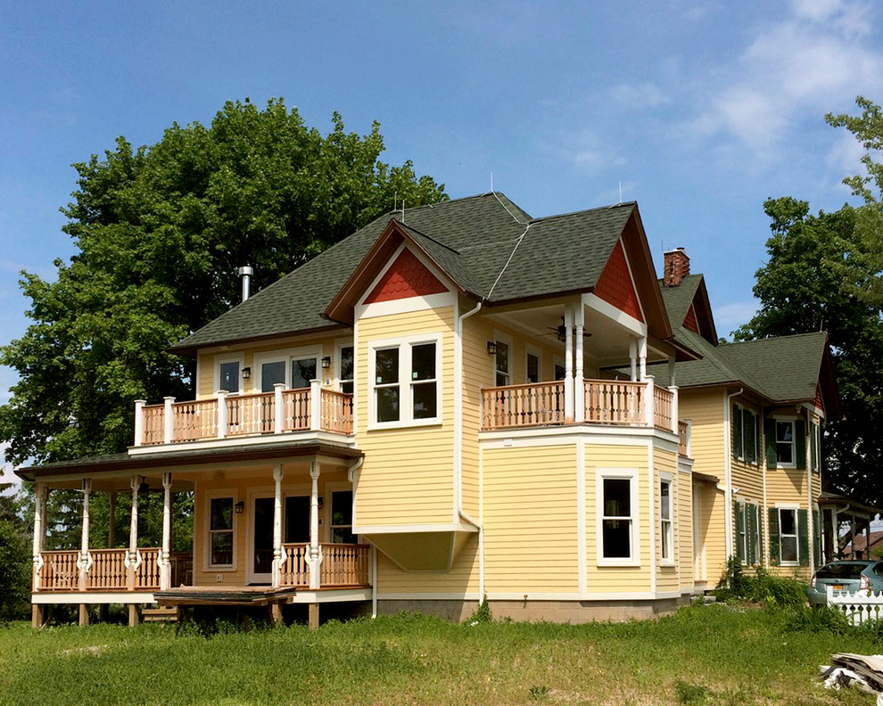 Ispirazione per la villa grande gialla vittoriana a due piani con rivestimento in vinile, tetto a padiglione e copertura a scandole