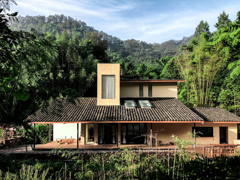 Modelo de fachada de casa beige tropical grande de dos plantas con tejado a dos aguas, revestimiento de estuco y tejado de teja de madera