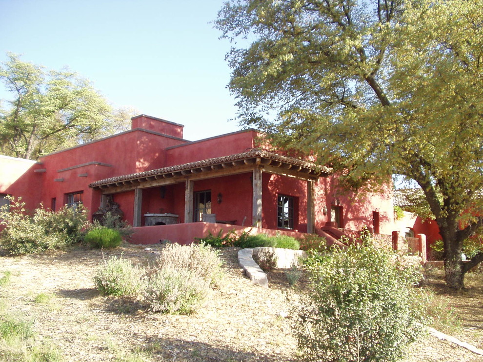 Réalisation d'une façade de maison rouge chalet en stuc de taille moyenne et de plain-pied.