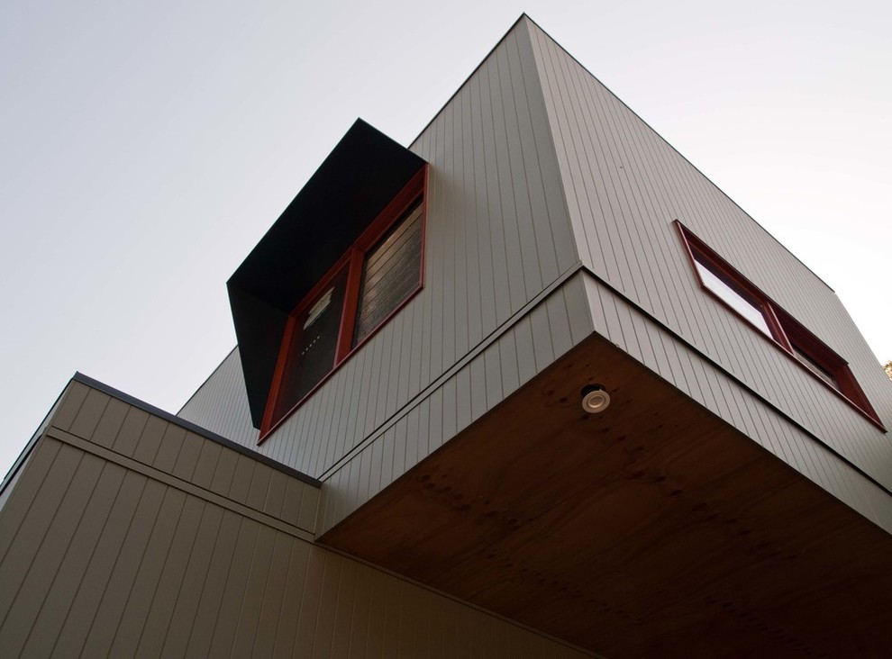 Réalisation d'une façade de maison beige vintage en bois à un étage avec un toit plat et un toit en métal.