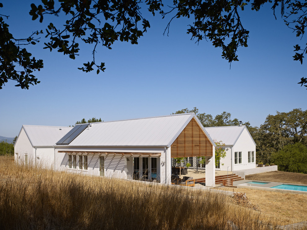 Diseño de fachada blanca de estilo de casa de campo grande de una planta con revestimiento de madera y tejado a dos aguas