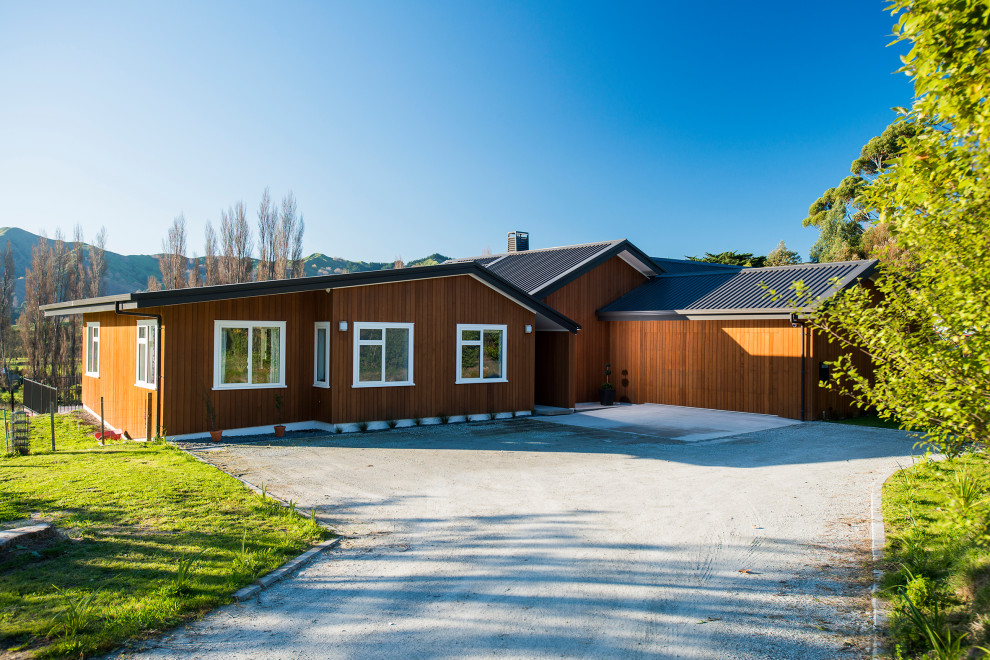 На фото: одноэтажный, деревянный, коричневый частный загородный дом среднего размера в стиле модернизм с двускатной крышей и металлической крышей с