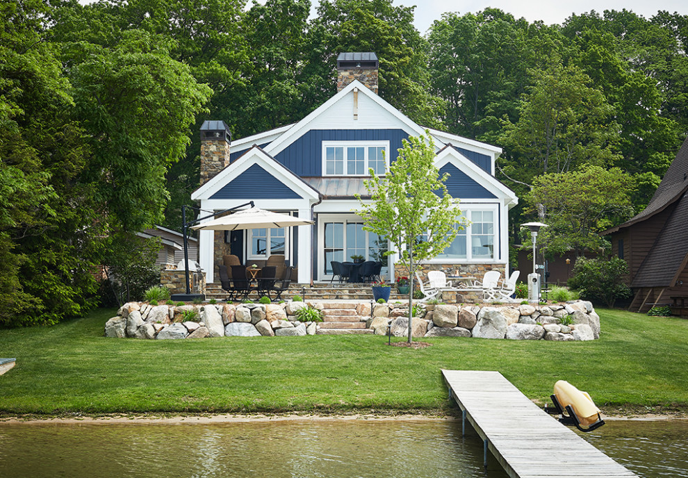 На фото: двухэтажный, синий частный загородный дом в морском стиле с двускатной крышей
