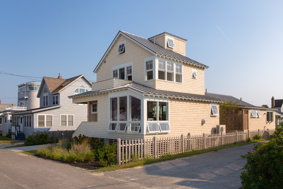This is an example of a medium sized and beige coastal house exterior in Portland Maine with three floors, wood cladding and a pitched roof.