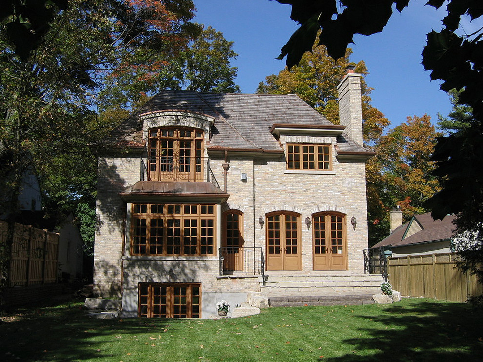 Cette photo montre une grande façade de maison beige chic en brique à un étage avec un toit à quatre pans et un toit en shingle.