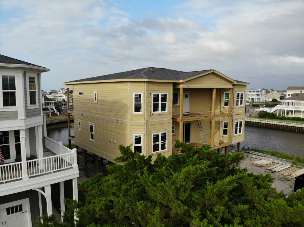 На фото: большой, трехэтажный частный загородный дом в морском стиле с облицовкой из ЦСП, вальмовой крышей и крышей из гибкой черепицы