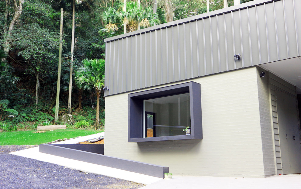 Cette image montre une façade de maison métallique et grise minimaliste de taille moyenne et à un étage avec un toit plat et un toit en métal.