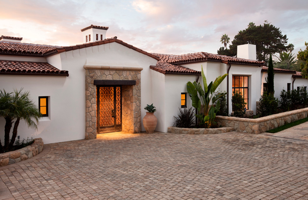 Cette image montre une façade de maison blanche méditerranéenne en stuc de plain-pied avec un toit à deux pans et un toit en tuile.