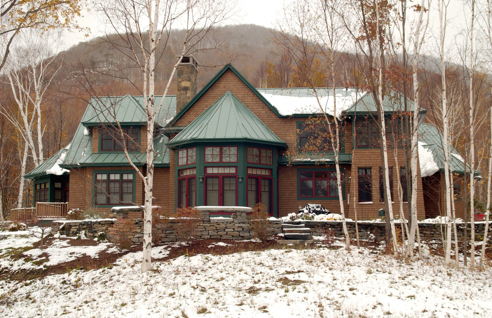 Réalisation d'une grande façade de maison marron chalet en bois à un étage avec un toit à quatre pans et un toit en métal.