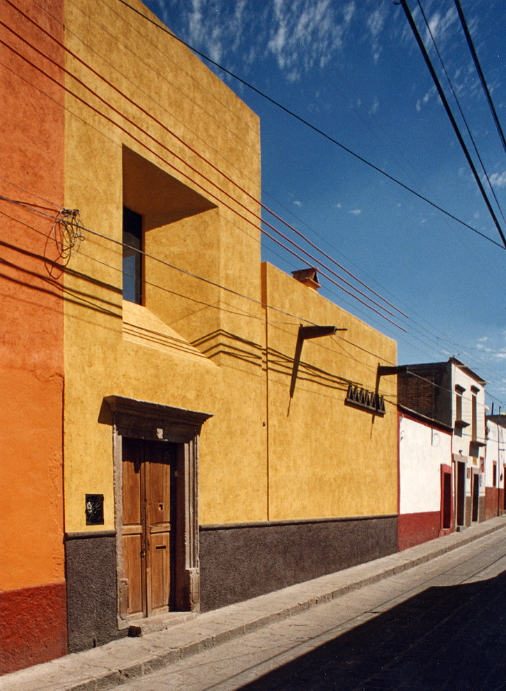 Imagen de fachada amarilla tropical pequeña con revestimiento de estuco y tejado plano