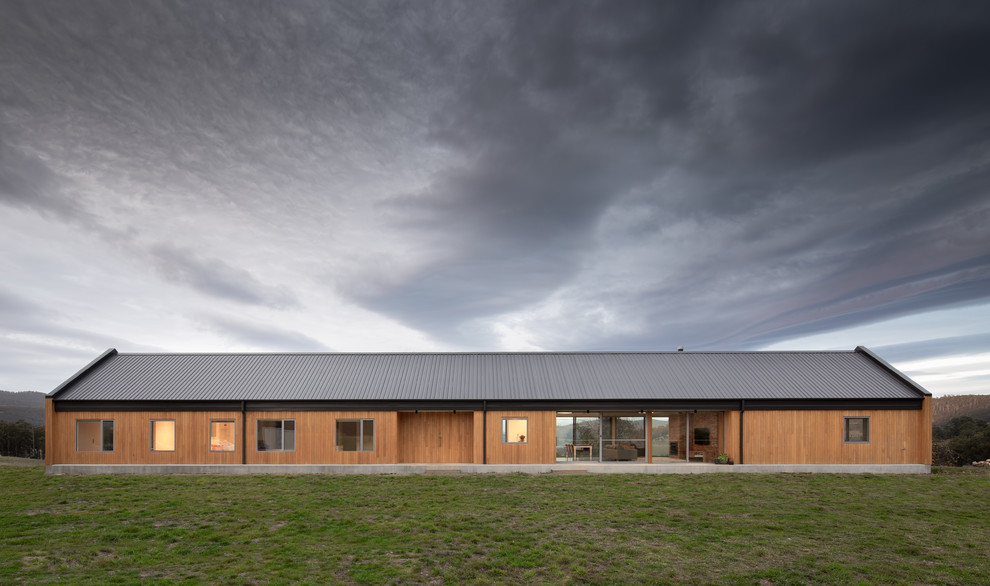 Diseño de fachada de casa beige campestre grande de una planta con revestimiento de madera, tejado a dos aguas y tejado de metal