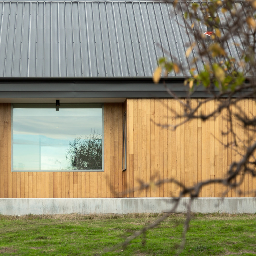 Réalisation d'une grande façade de maison beige champêtre en bois de plain-pied avec un toit à deux pans et un toit en métal.